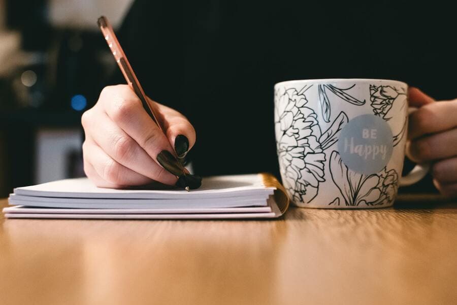 Close up of woman's hand writing in notebook with coffee cup