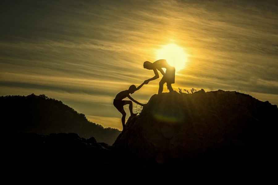 one person helping another climb up a hill 